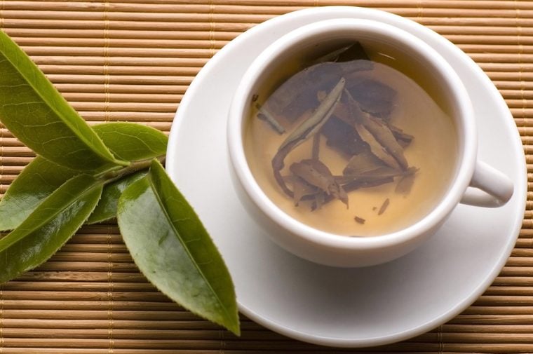 a cup of green tea with fresh leaves on the bamboo tray