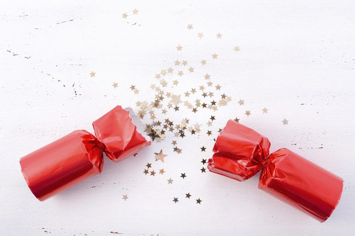 Festive surprise concept with opened red bon bon Christmas cracker and glitter stars on white wood table with copy space for your text here. 