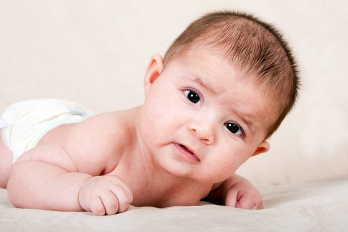 Cute Caucasian Hispanic baby infant laying on belly lifting head making funny expression.