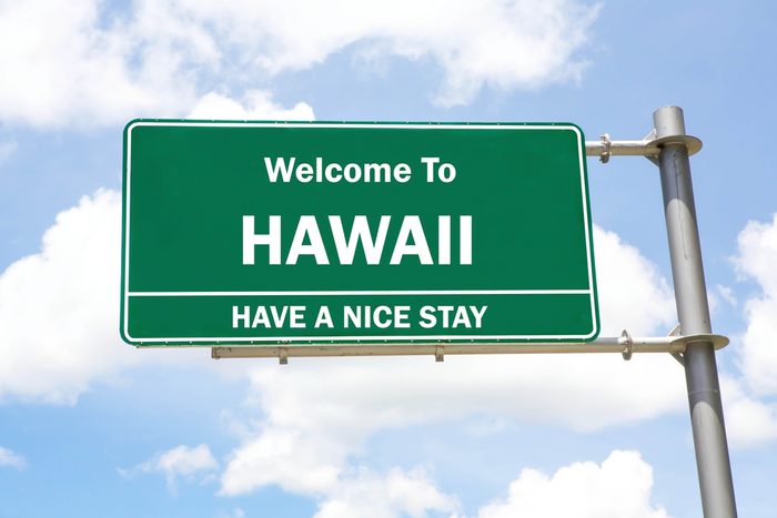 Green overhead road sign with a Welcome to Hawaii, Have a Nice Stay concept against a partly cloudy sky background.