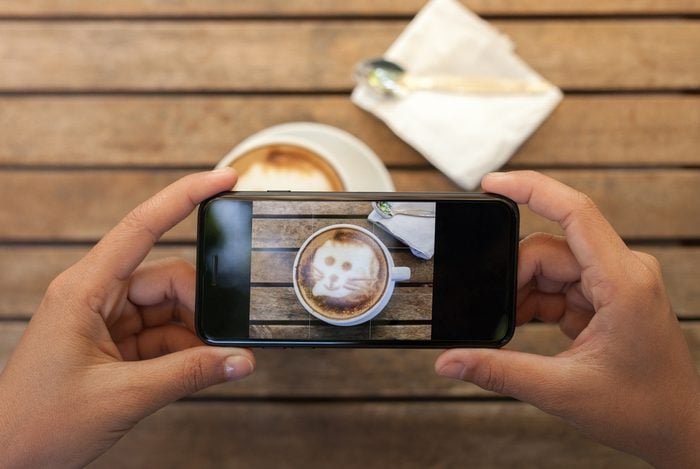 overhead view of hands holding a smartphone taking a photo of a coffee cup