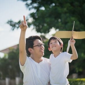 Asian father and son playing cardboard airplane together in the park outdoors
