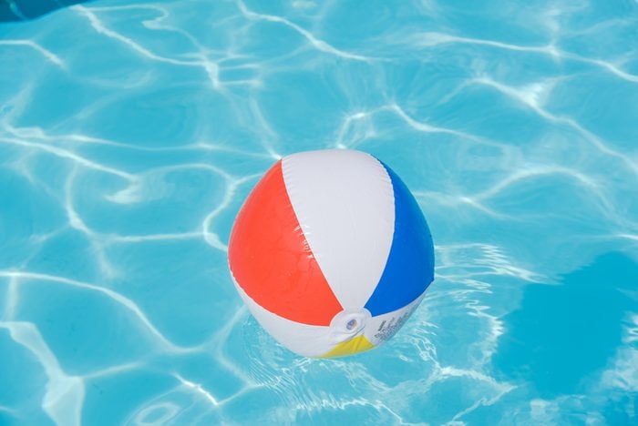 Bright multicolor beach ball floating in blue swimming pool, colorful float in a refreshing blue swimming pool with waves reflecting in the summer sun. Active vacation background. Lifesaver for kid.