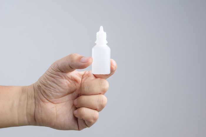 Hand holding eye or ear drop bottle on white background