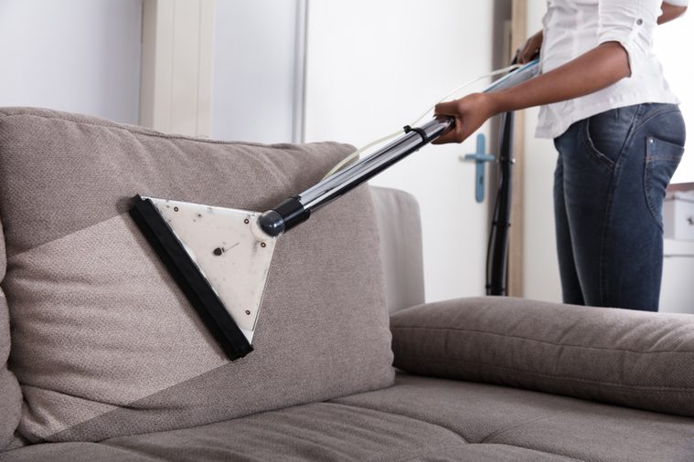 Housewife's Hand Cleaning Sofa With Vacuum Cleaner At Home