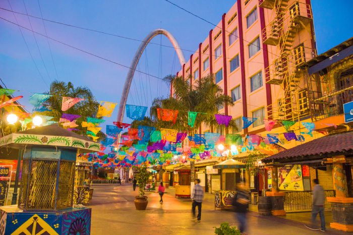 TIJUANA, MEXICO - APRIL 26, 2017: Santiago Arguello pedestrianized shopping and bars street with festival flags above, millennial arch (el arco y reloj monumental) and blurred motion silhuettes