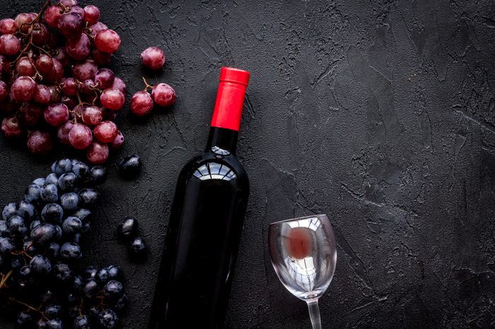 Taste red wine. Bottle of red wine, glass and black grape on black stone background top view copyspace