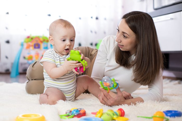 Funny baby boy and young woman playing in nursery. Happy family having fun with colorful toys at home.