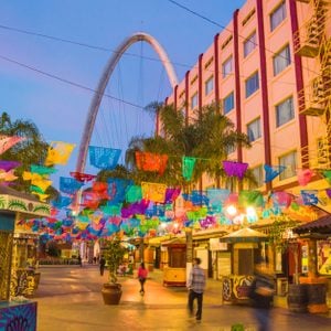 TIJUANA, MEXICO - APRIL 26, 2017: Santiago Arguello pedestrianized shopping and bars street with festival flags above, millennial arch (el arco y reloj monumental) and blurred motion silhuettes