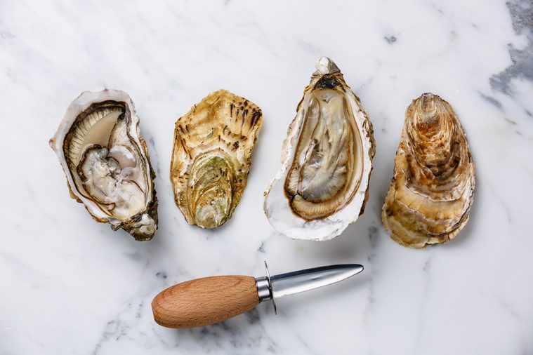 Shucked Oysters Fines de Claire and oyster knife on white marble background
