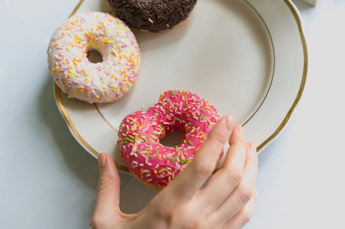 A girl's hand takes a donut from a plate with a pink chocolate frosting. View from above