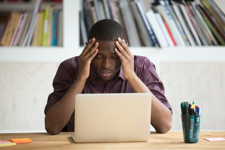 Frustrated black man feeling depressed after fail, upset african-american businessman sitting in front of laptop stressed about bankruptcy debt, dark-skinned guy suffering from headache migraine