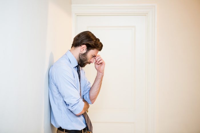 Worried man with hand on forehead leaning on wall at home