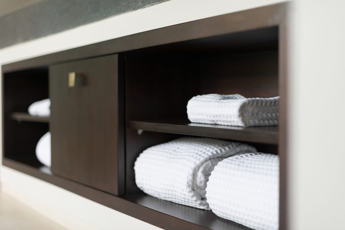 Wall with built in wooden shelf. Neat stack of white soft towels in bathroom. Closet with clean folded textile for spa and hygiene. Modern interior of hotel room. Luxury resort with classic design.