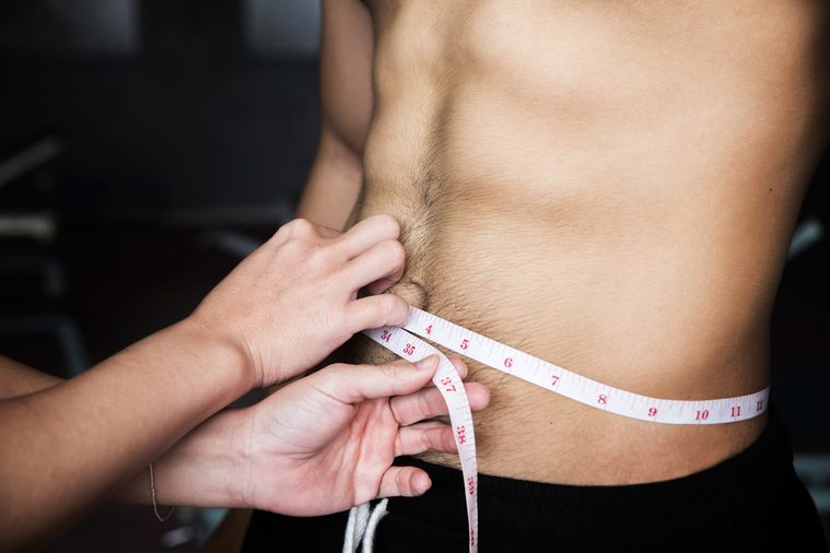 Close up hands women measure men's waist with tape measure at the gym.