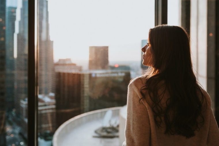  Young woman sitting at window enjoying the city skyline from the 35 floor at sunset with stunning panoramic view of Los Angeles.