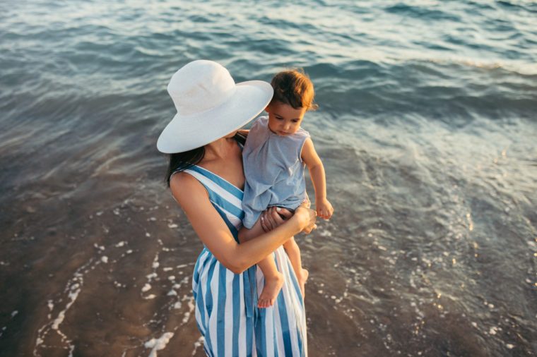 View from above of young mother kiss daughter at the sea sunset and beach background. Family vacation. Travel. Caucasian happy female with baby outside at ocean sunset. Motherhood love