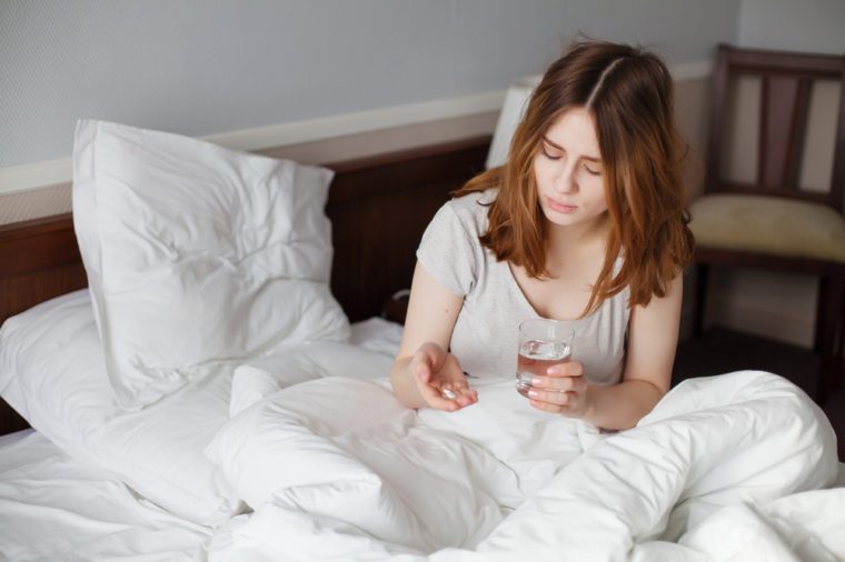 Girl On Bed Taking Pill With Water Glass In Bedroom