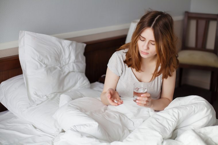 Girl On Bed Taking Pill With Water Glass In Bedroom