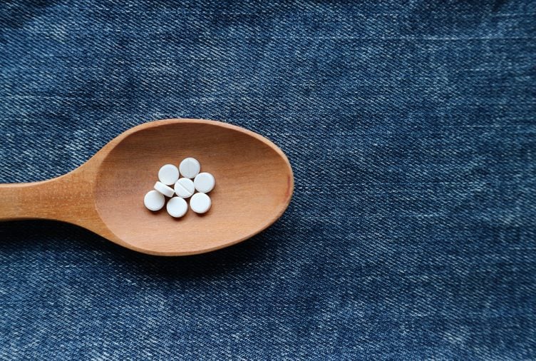 White round pills medicine on wood spoon on blue jeans denim background with empty space