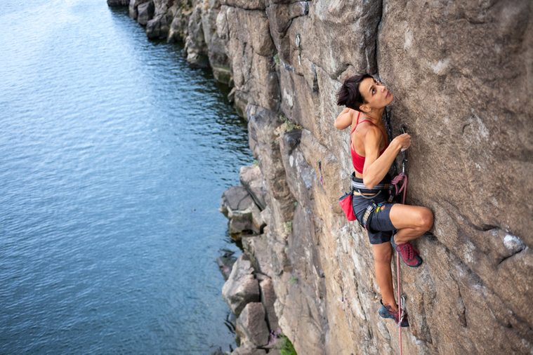 The girl climbs a climbing route over the water. extreme travel. Sport in nature.