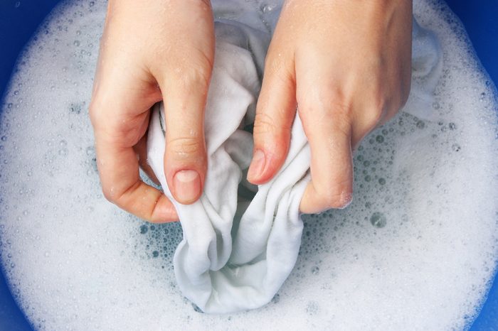A woman washes clothes by hand in soapy water.