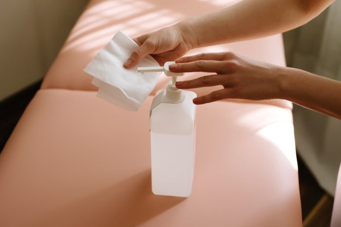 Woman hands pushing pump plastic white bottle on white napkin indoor. top view