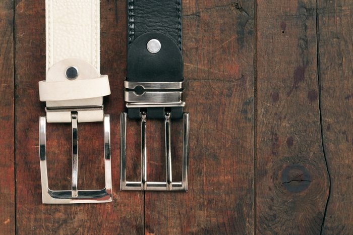 White and black leather belts hanging on old wooden background