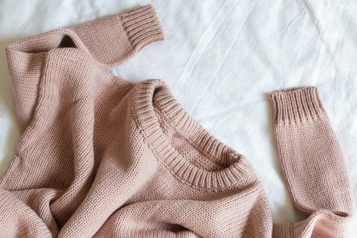 pink knitted sweater lies on a white blanket
