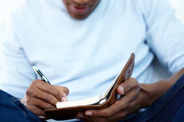 Close-up of young African man writing something in notepad