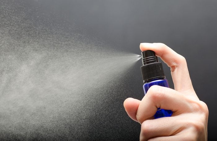 Woman hand 's holding bottle spray against gray background