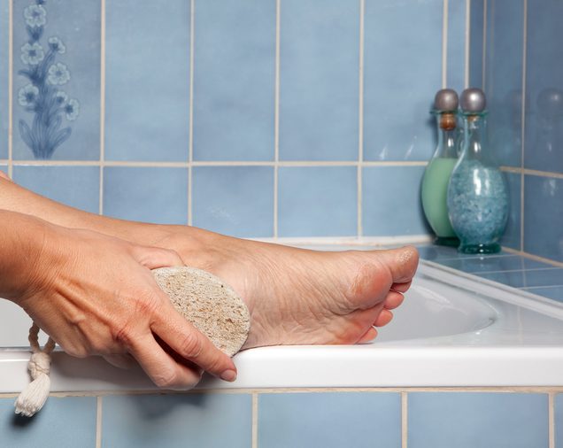 Hand removing callus from feet using pumice stone