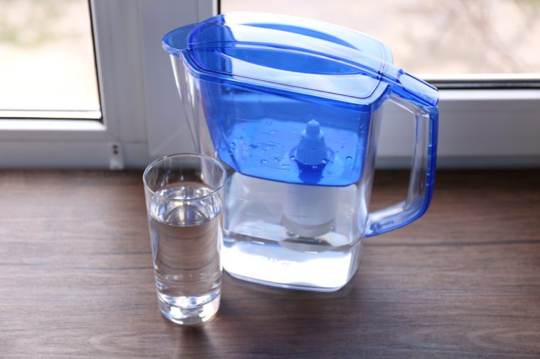 Water filter jug and a glass on the wooden windowsill