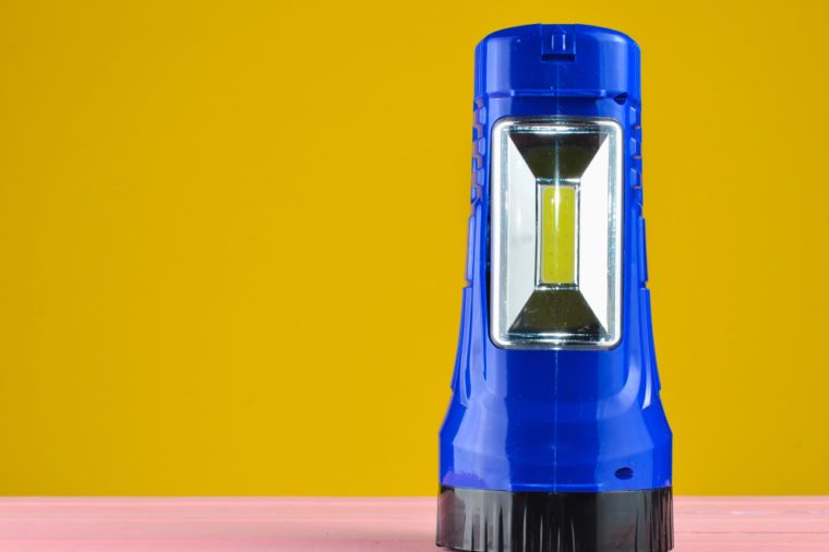 Blue flashlight projector lies on a desk isolated on a yellow wall