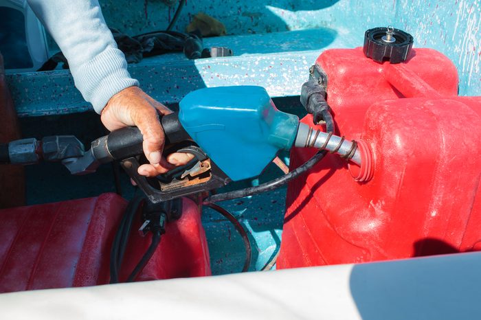 Close-up shot of a man fueling red plastic tank of a motor boat with petrol
