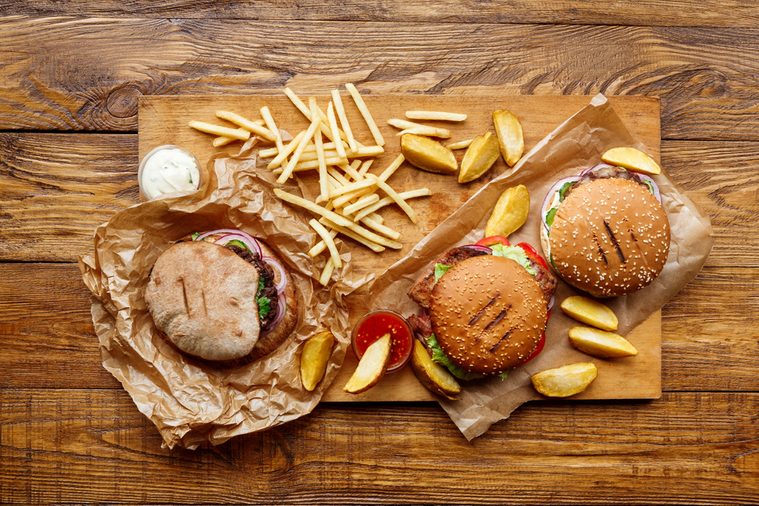 Fast food dish top view. Meat burger, potato chips and wedges. Take away composition. French fries, hamburger, mayonnaise and ketchup sauces on wood. Menu or receipt background