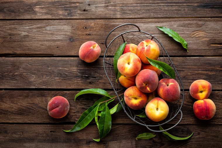 Fresh peaches fruits with leaves in basket on dark wooden rustic background, top view