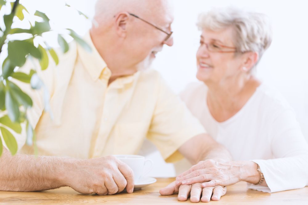 Happy, blurred elder couple sitting at a table and holding hands