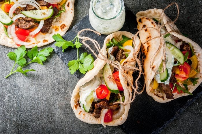 Healthy snack, lunch. Traditional Greek wrapped sandwich gyros - tortillas, bread pita with a filling of vegetables, beef meat and sauce tzatziki. On black stone table Copy space 