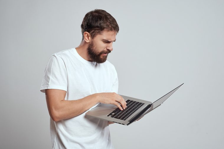  serious man with a beard working behind a laptop on a gray background 