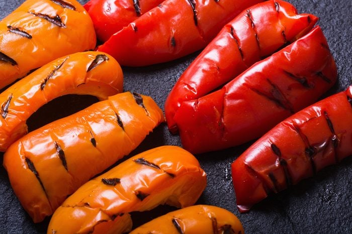 Orange and red grilled peppers on black stone .