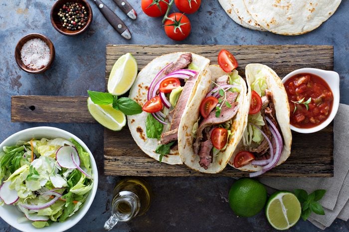 Steak tacos with sliced meet, salad and tomato salsa on a cutting board