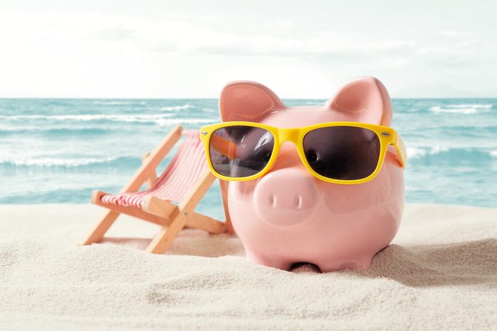 Piggy bank with sunglasses on a beach next to a beach chair
