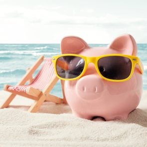 Piggy bank with sunglasses on a beach next to a beach chair