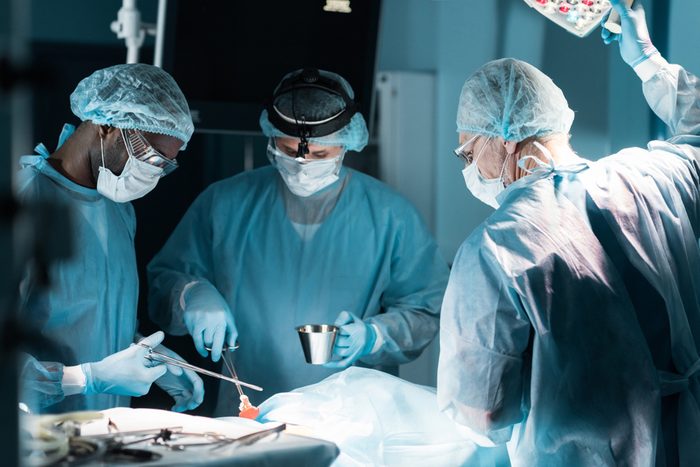 multiethnic surgeons in medical masks operating patient in operating room