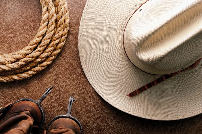 American West rodeo cowboy traditional white straw hat with roping lasso rope and vintage western riding spurs on brown leather boots over hide background