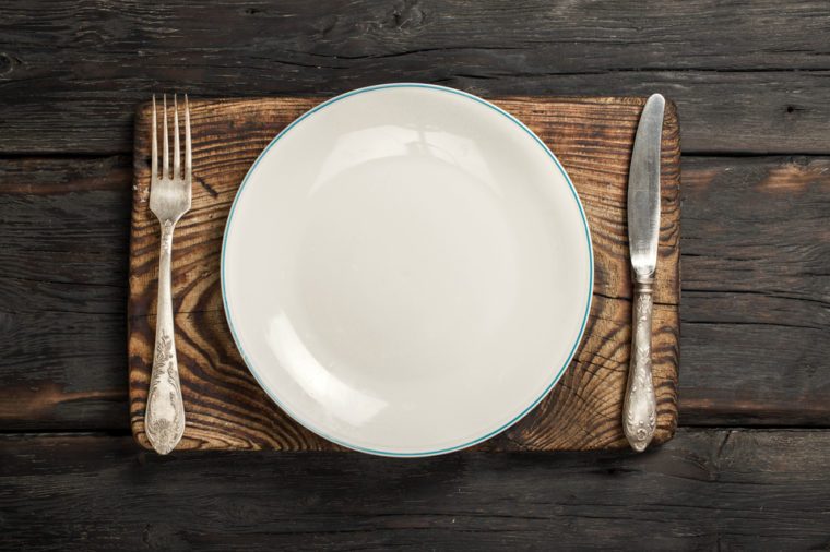 White empty plate with fork and knife on a old wooden board on a dark wooden background, top view