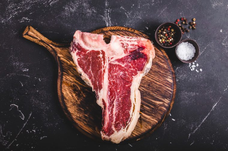 Raw marbled meat steak T-bone, spices, wooden cutting board, rustic stone background.  Beef T-bone steak, ready to cook.  Top view.  Ingredients for roasting meat.  T bone steak.  Meat steak concept
