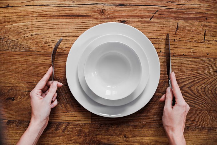 Healthy food theme: hands holding knife and fork on a plate, top view