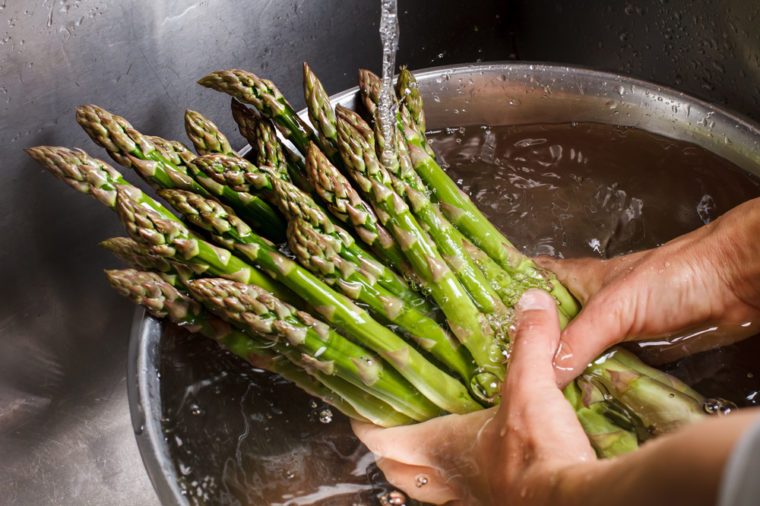 Man's hands washing asparagus. Asparagus under flow of water. Greenery bought at farmer's market. Food high on vitamins.